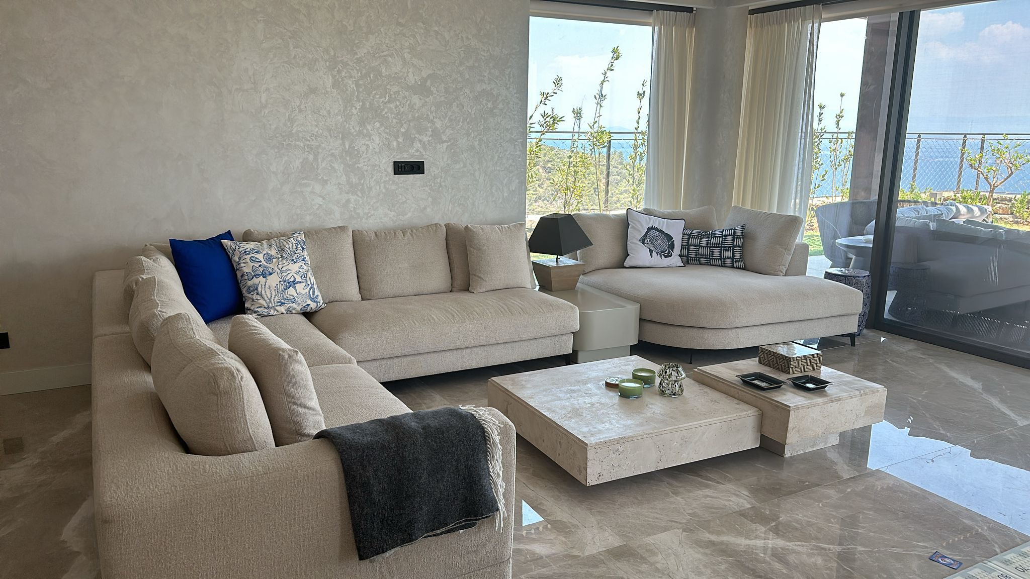 Living room in the Seba project, Gölköy, Bodrum: beige L-shaped sofa and block travertine coffee tables in front of sea-view glazing