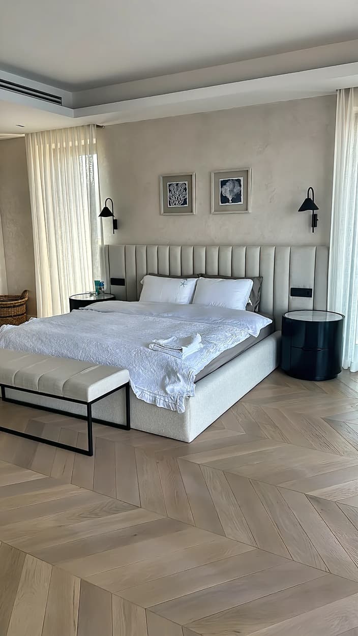 Bedroom in the Seba project, Gölköy, Bodrum: wall-to-wall channel-tufted upholstered headboard, upholstered bed, black round nightstands and an upholstered bench on a black metal frame
